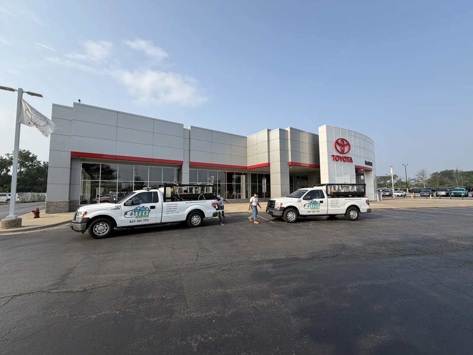 Two branded Oleksy Services trucks and crew at the McGrath Toyota dealership in Elmhurst for a commercial exterior cleaning