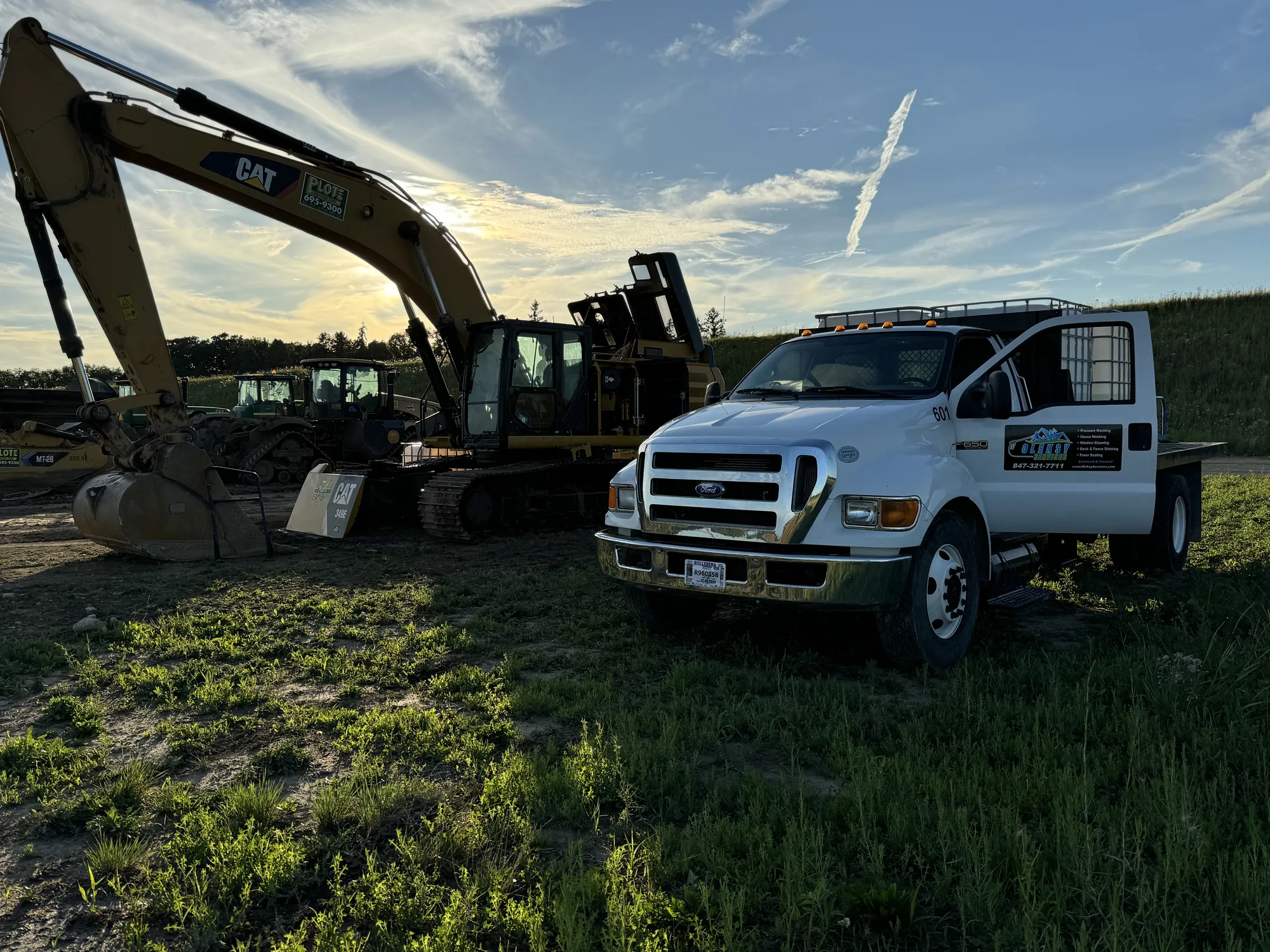 Oleksy Services F-650 flatbed service truck parked beside a CAT excavator and heavy construction equipment at a jobsite