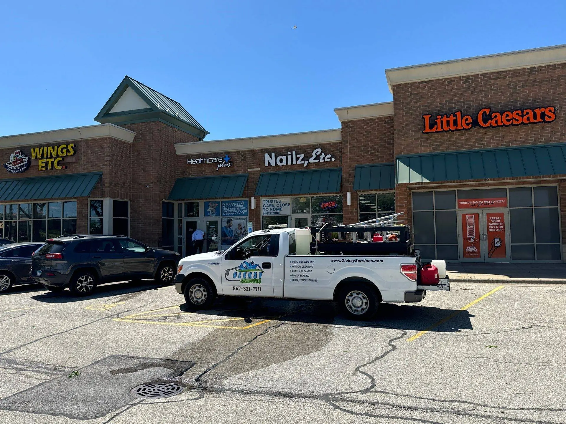 Oleksy Services truck parked in front of a retail strip mall storefront
